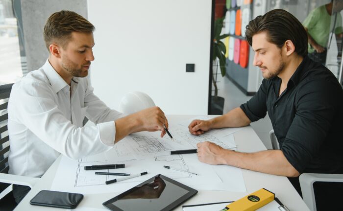 Two engineering working together and using digital tablet looking blueprint and analysis with architectural plan on desk