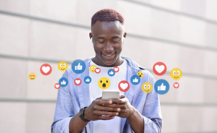 Smiling attractive millennial afro american guy in wireless headphones chatting online on phone, on social networks
