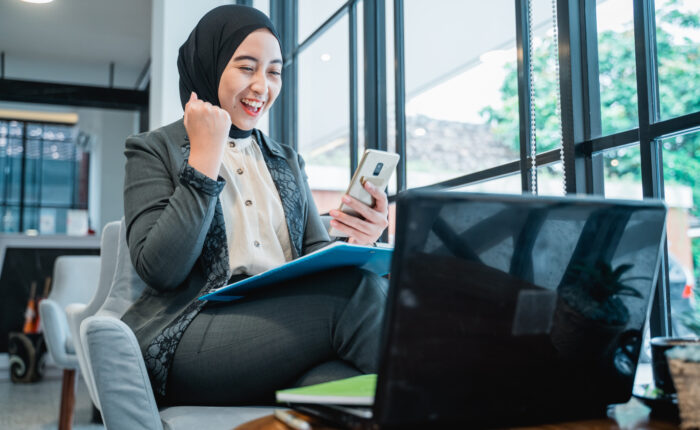 excited muslim woman raise her arm while looking at her phone